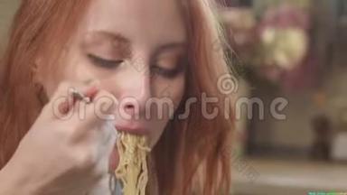漂亮的红发女孩在厨房里用叉子吃方便面。 吃塑料盒子里的垃圾食品。 坏坏坏坏